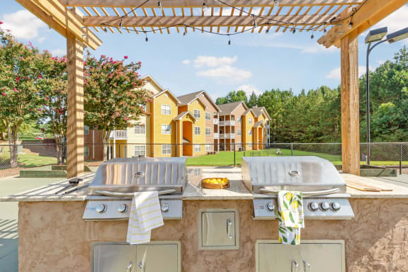 a patio with a grill and two chairs under a pergola