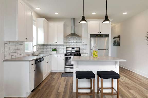 A modern kitchen with white cabinets and a wooden floor.
