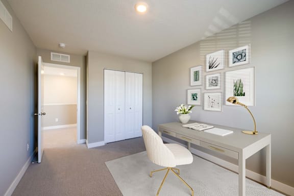 A white chair is in front of a desk with a lamp on it.