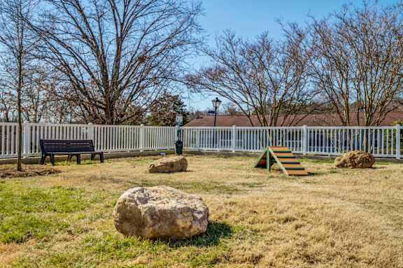 A large rock sits in the middle of a grassy area with a white fence and bench in the background.