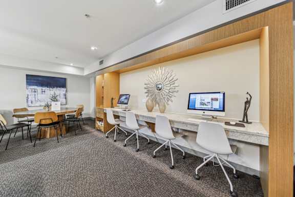 A room with a long desk and chairs, a computer on the desk, and a large sunburst mirror on the wall.