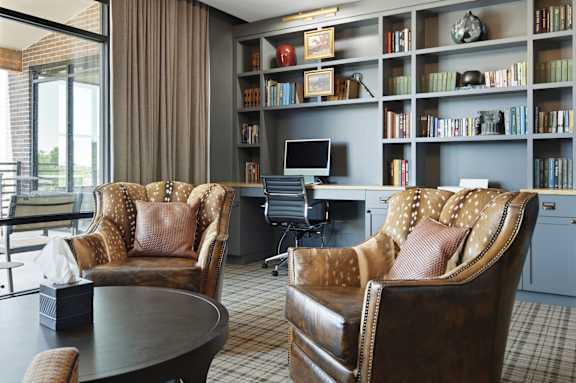 Two leather chairs with a desk and bookshelf in the background.