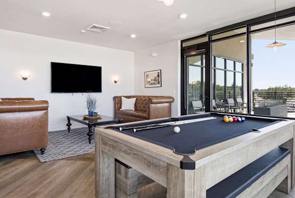 A pool table is in the middle of a room with leather chairs and a television.