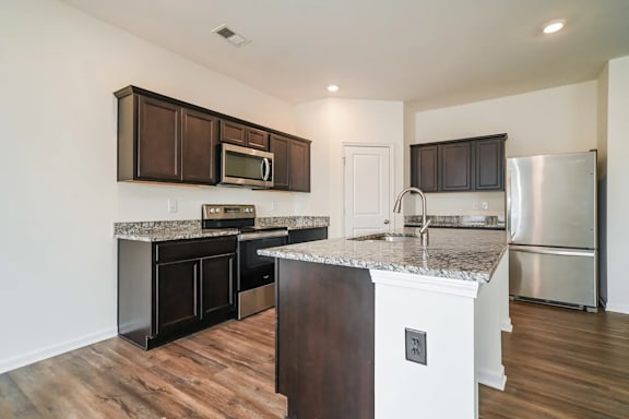 A kitchen with dark brown cabinets and a granite countertop.