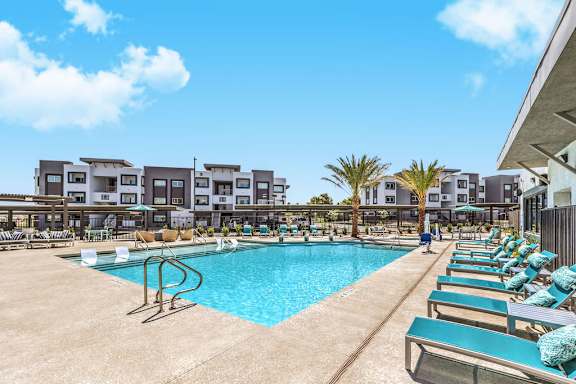 A swimming pool surrounded by lounge chairs and a building in the background.