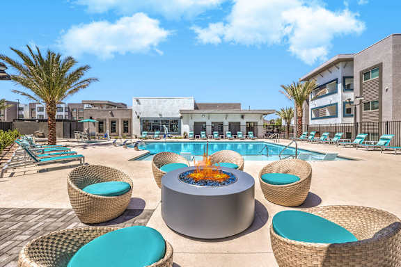 A pool area with a fire pit surrounded by wicker chairs.