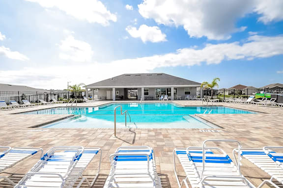A pool with sun loungers and a building in the background.