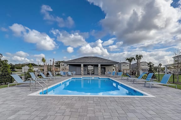 A swimming pool surrounded by lounge chairs and a building in the background.