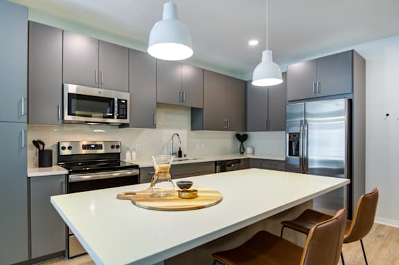 A modern kitchen with a white island and brown chairs.