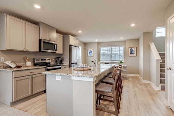 A kitchen with a long counter and a staircase in the background.