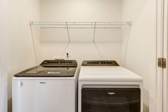Two white and one black washing machine in a laundry room.