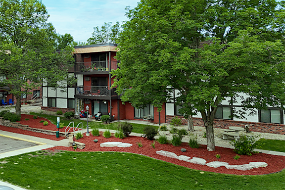 A red building with a balcony and a tree in front.