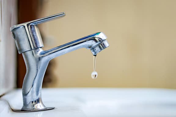 A silver faucet with a single drop of water dripping from it.