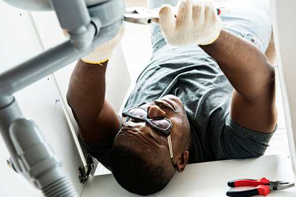 A man is fixing a sink with a wrench.