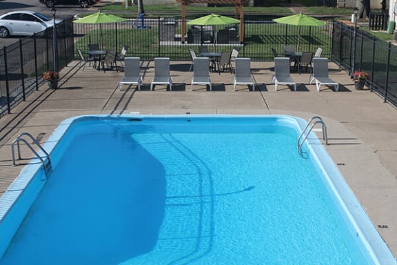 a large swimming pool with a sundeck area with chairs and umbrellas
