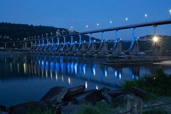 a row of blue lights on a bridge over a river at night