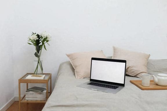 a laptop computer sitting on a bed with a vase of flowers
