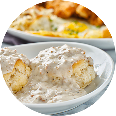 A white bowl filled with biscuits covered in gravy.
