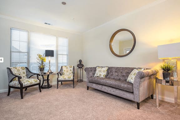 A living room with a grey couch, two chairs, and a table with a lamp.