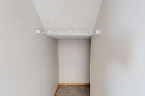 A closet with a white shelf on top and a brown floor.