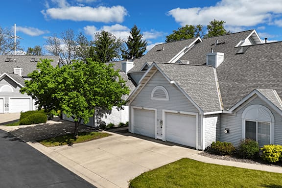 A house with a grey roof and white walls with a driveway leading to a garage in front.