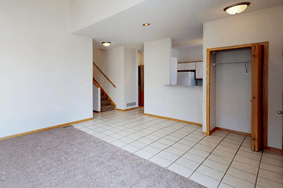 A room with a carpeted floor and a staircase in the background.
