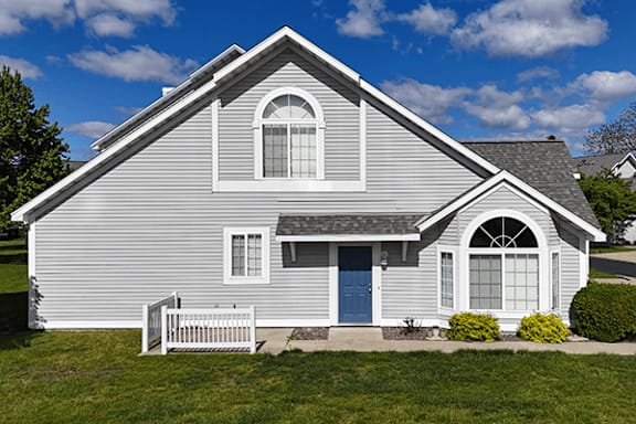 A grey house with a white fence sorrounding a small patio and blue door