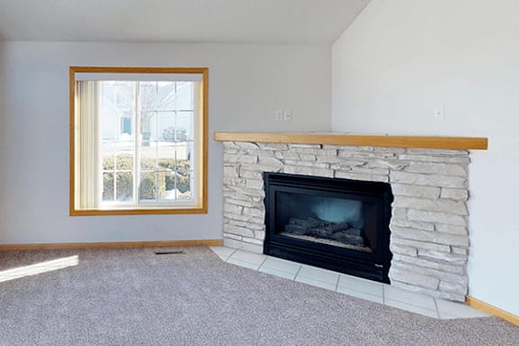 A stone fireplace with a wood mantle and a fire going in it.