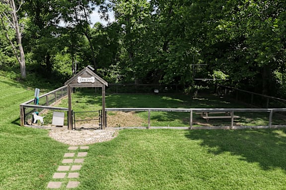 A small wooden shelter with a sign on top is surrounded by a metal fence and a grassy area.