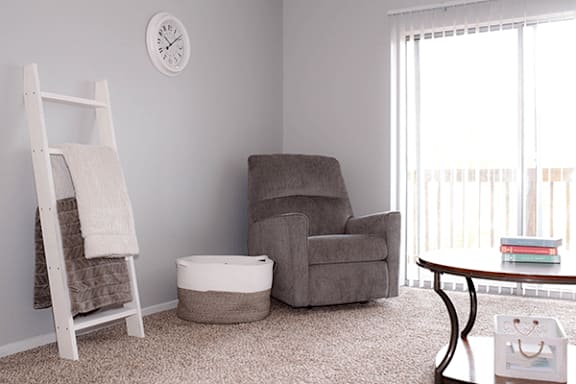 A grey chair sits in a room with a white ladder and a white ottoman.