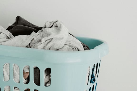 A light blue laundry basket filled with a grey and black pile of clothes.