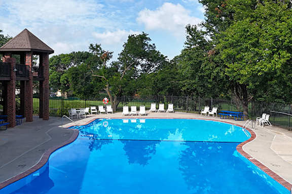 A large blue swimming pool surrounded by trees and chairs.
