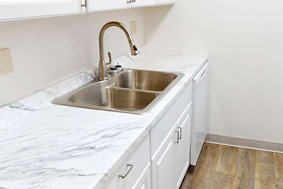 A kitchen with a marble countertop and a stainless steel sink.