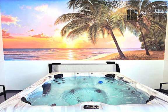A hot tub in the foreground with a beach scene on the wall behind it.
