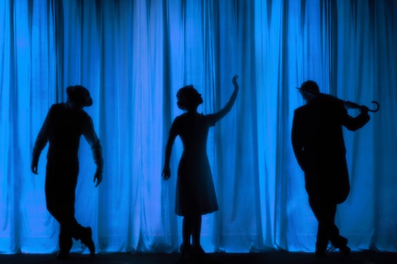 three actors are silhouetted in front of a blue curtain
