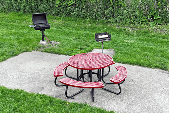 A red picnic table with a grill and a mailbox in the background.