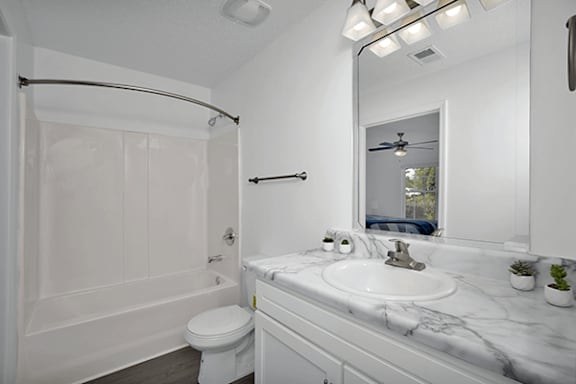 A white bathroom with a marble counter top and a white toilet.