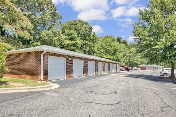 A parking lot in front of a brick building with trees in the background.