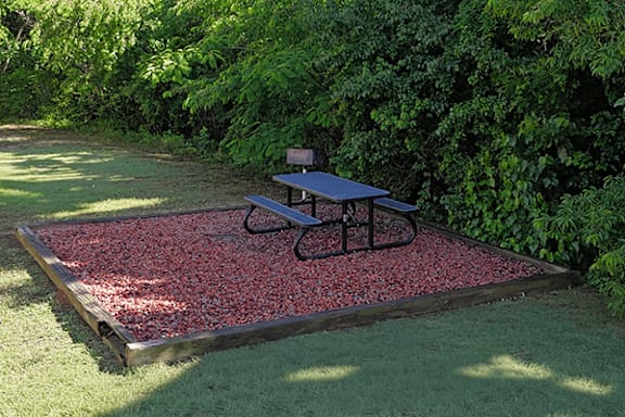 A picnic table is on a gravel platform in a grassy area.