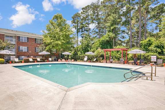 A large outdoor swimming pool surrounded by trees and a red pergola.