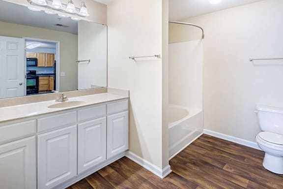 A white bathroom with wood flooring and a white toilet.