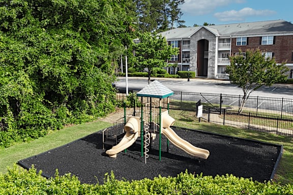 A playground with a slide and a green fence.