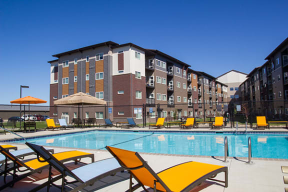a swimming pool with yellow chaise lounge chairs and umbrellas in front of an apartment