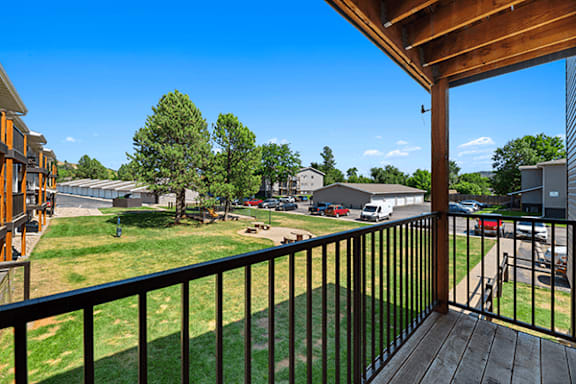 A balcony overlooks a grassy area with trees and a parking lot.