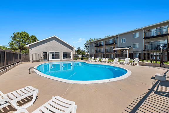 A pool surrounded by chairs and a building in the background.