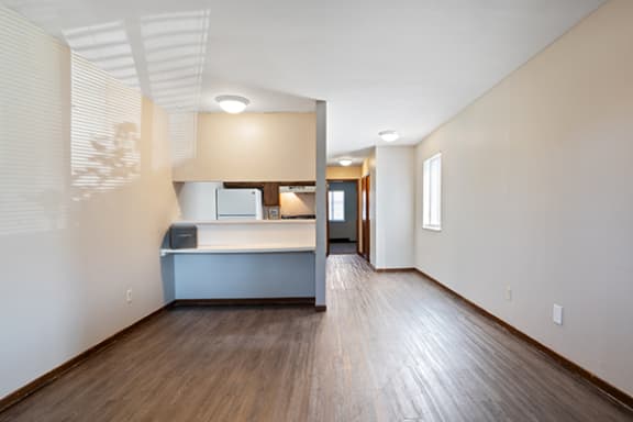 the living room and kitchen of an empty house with wood flooring and white walls