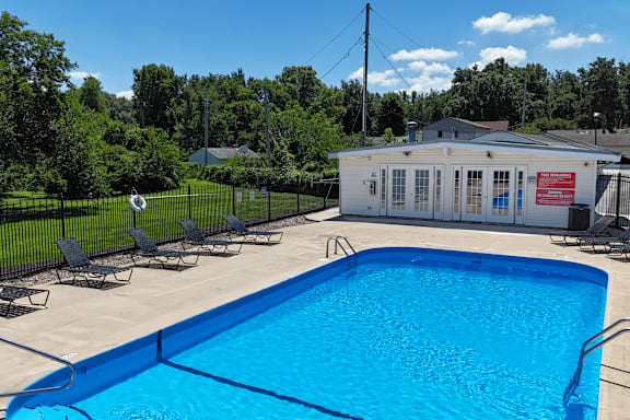 A blue swimming pool surrounded by a black fence and chairs.