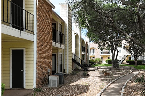A tree-lined walkway leads to a building with a black door.
