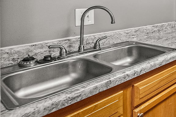 A kitchen sink with a marble countertop and wooden cabinets.
