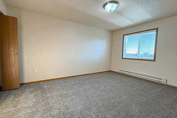 A room with a carpeted floor, a window, and a door.